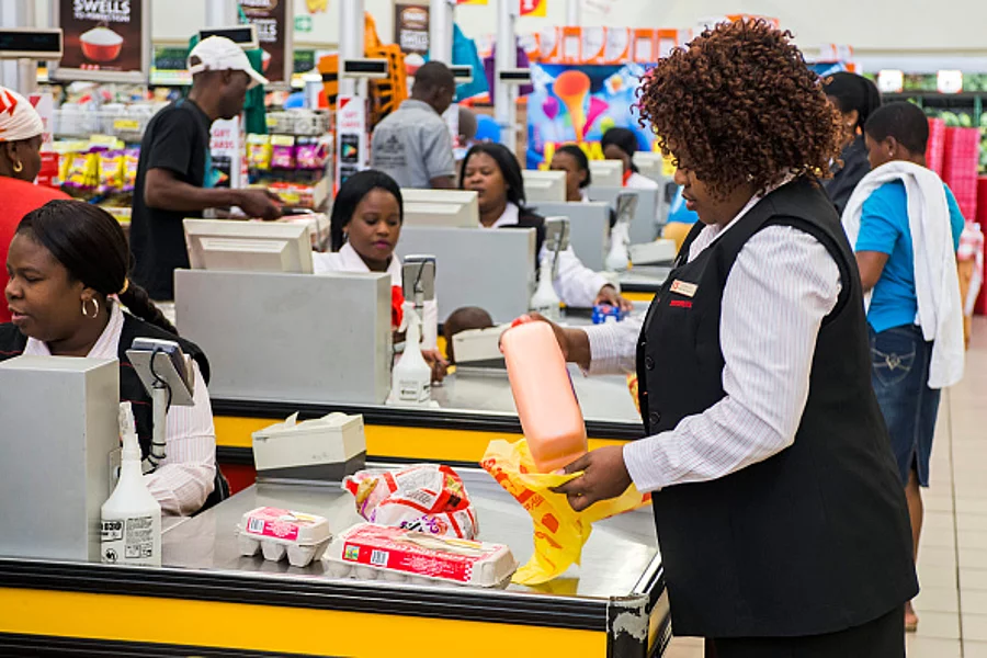 An employee packs a customer's bags with products as cashiers scan goods at the cash desks inside a Shoprite Holdings Ltd. supermarket in Alexandra district of Johannesburg,